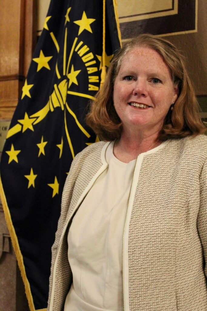 Cinde Wirth smiles while standing near the state flag of Indiana