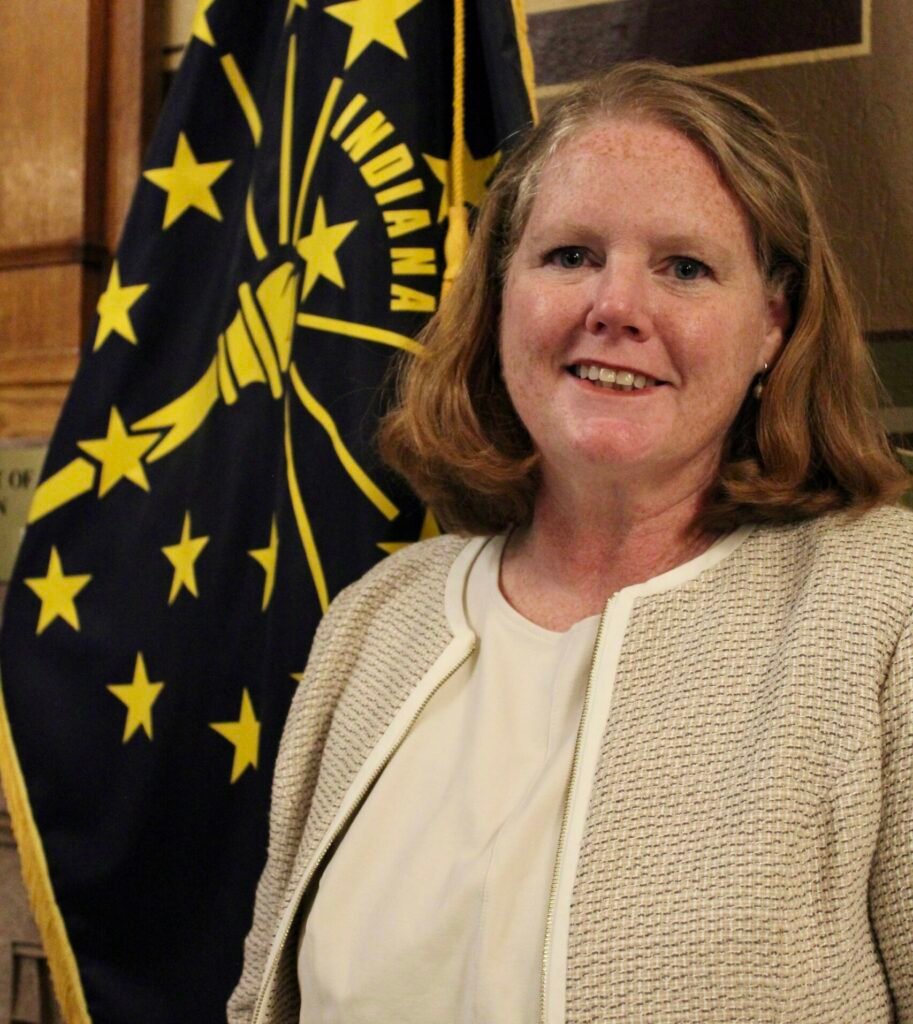 Cinde Wirth smiles while standing near the state flag of Indiana