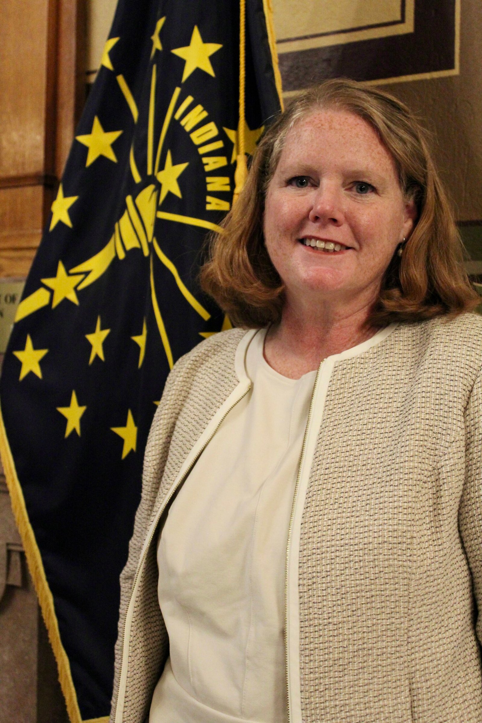 Cinde Wirth smiles while standing near the Indiana state flag